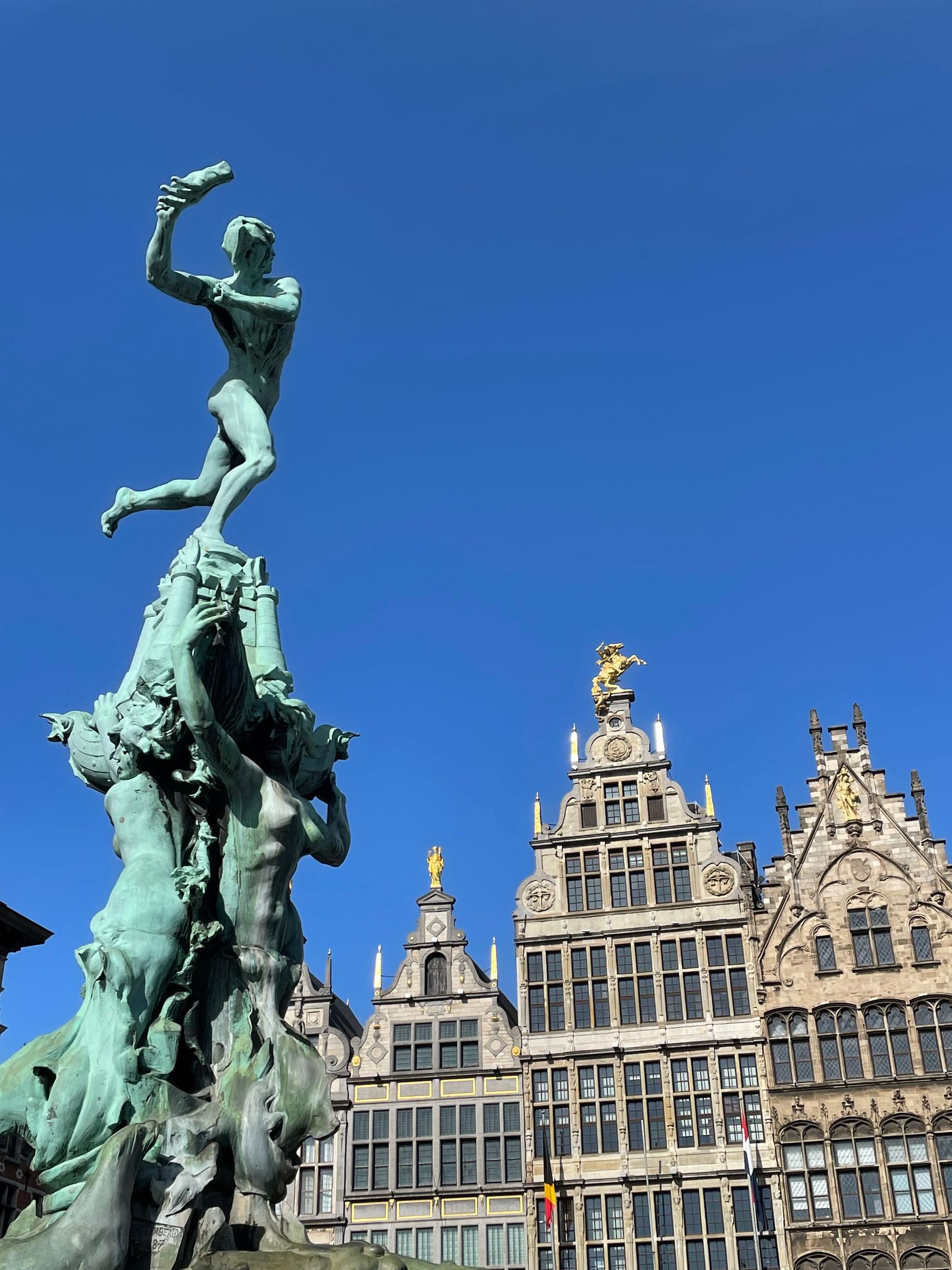 The Brabo Fountain in Antwerp: a figure throwing a hand, guildhalls behind, blue sky