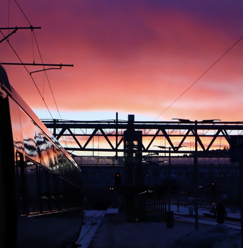 Magenta and orange sunset over a snowy train platform, the side of a train in frame