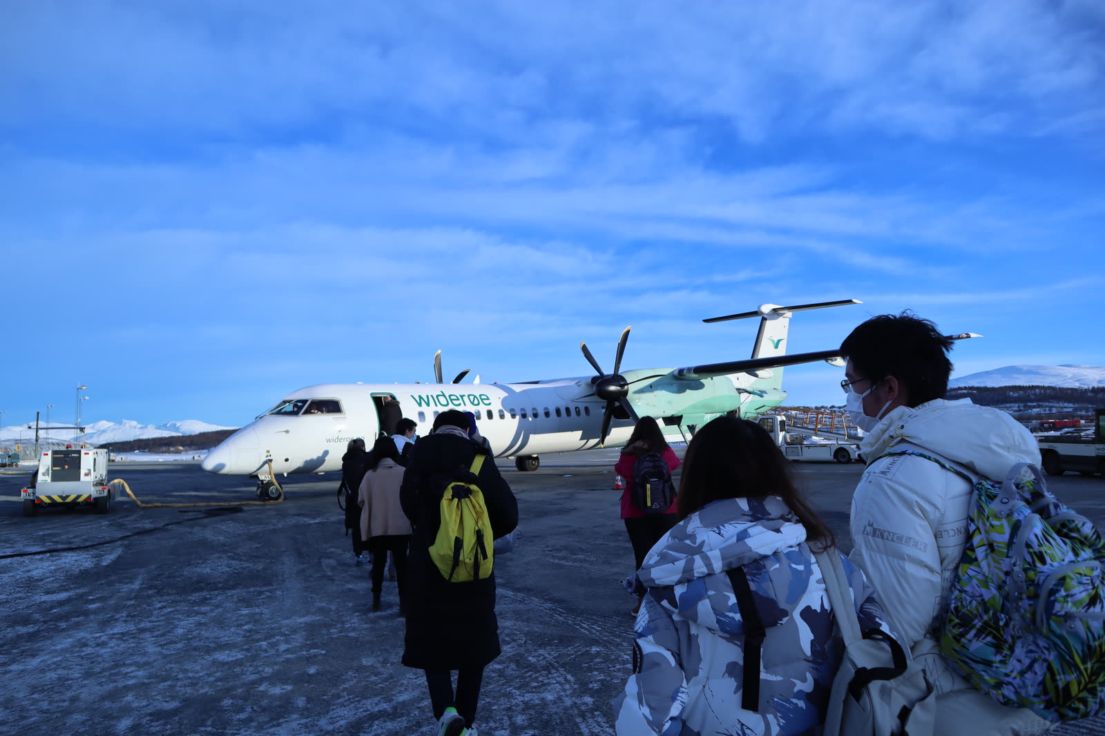 A person walking toward a Widerøe turboprop on a snowy tarmac under a clear blue sky
