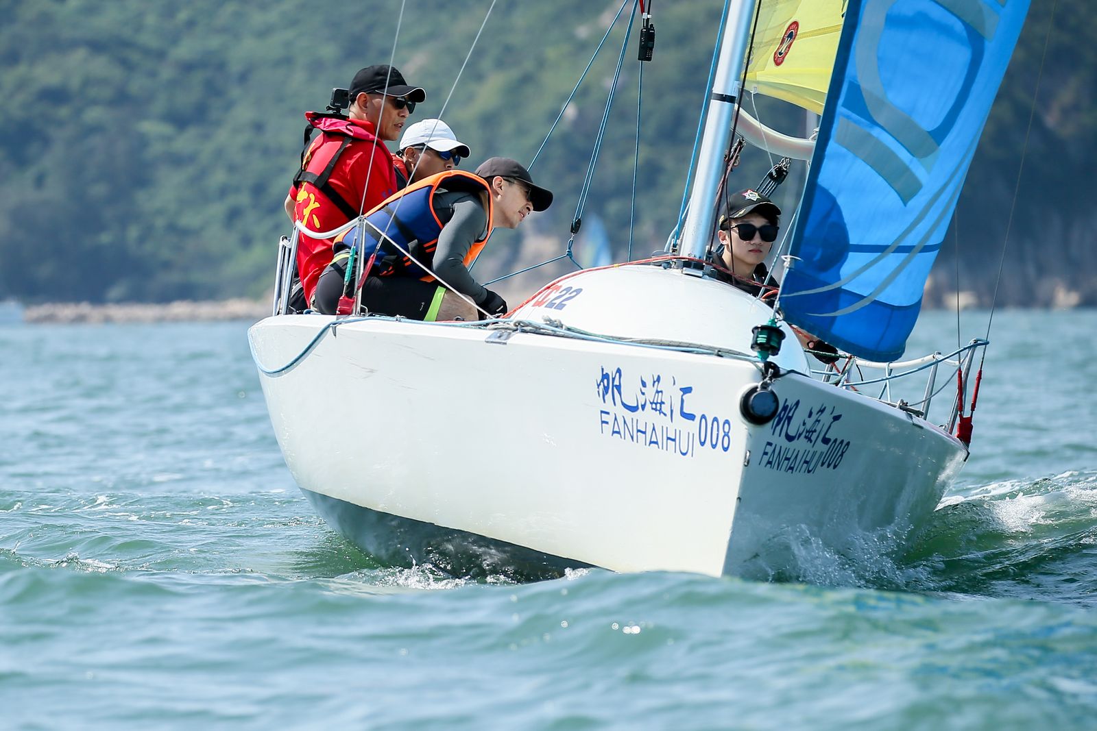 A white dinghy lettered 帆海汇 008, crew in yellow life jackets on turquoise water, a green hillside behind