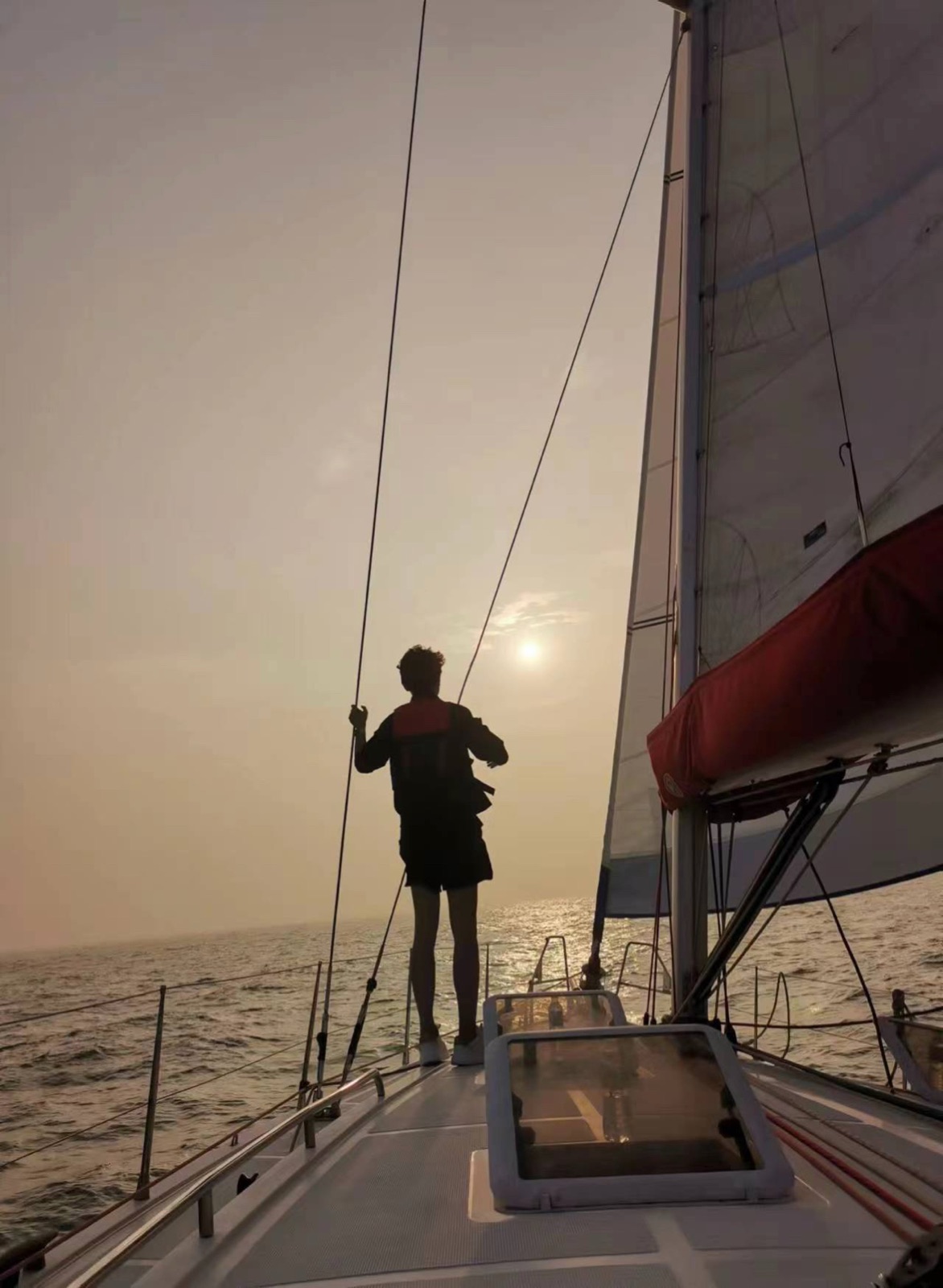 Silhouette of a sailor hauling a line on deck against the low sun