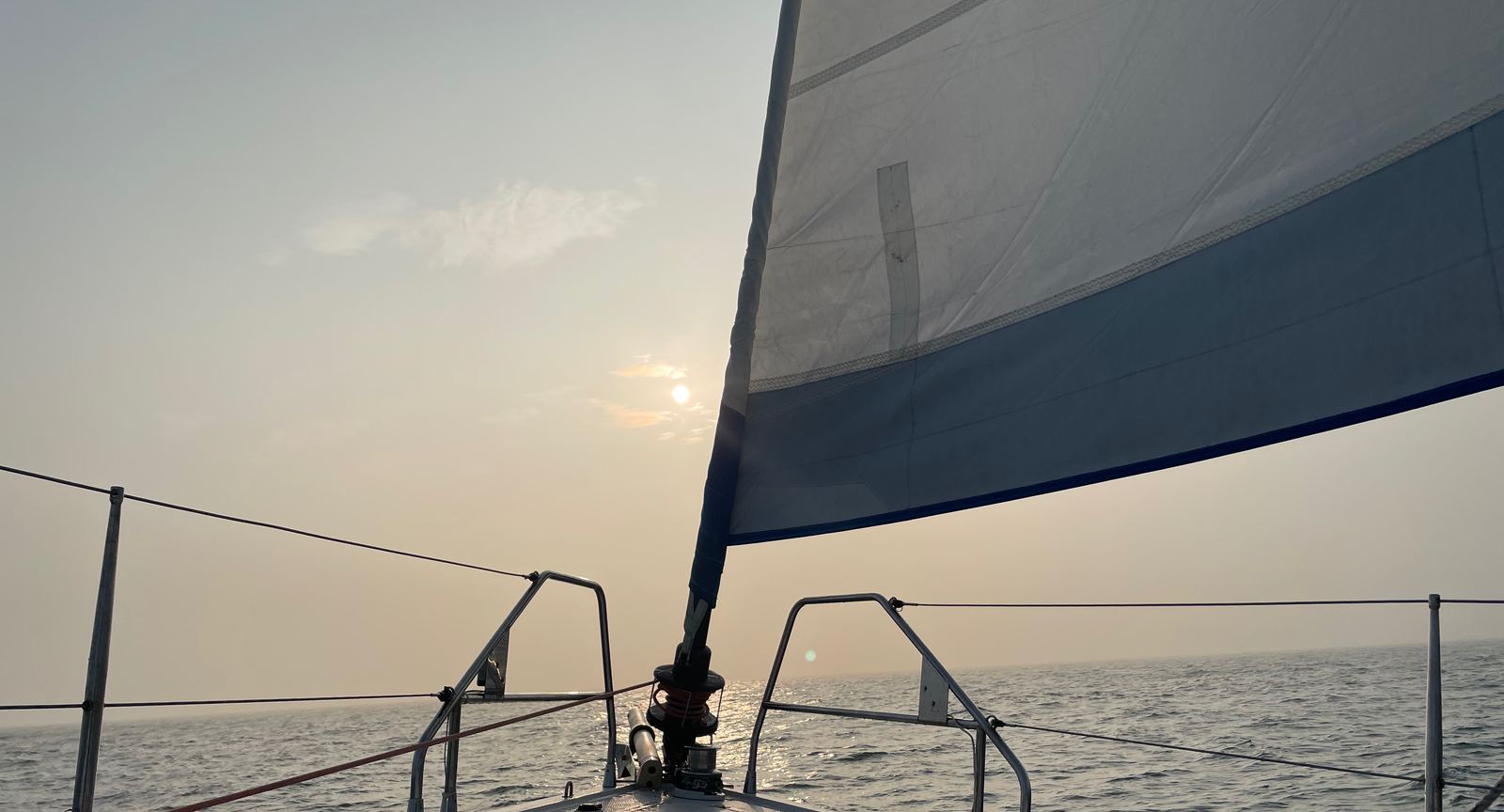 Sail and foredeck of a sailing yacht against the sunset, golden water beyond